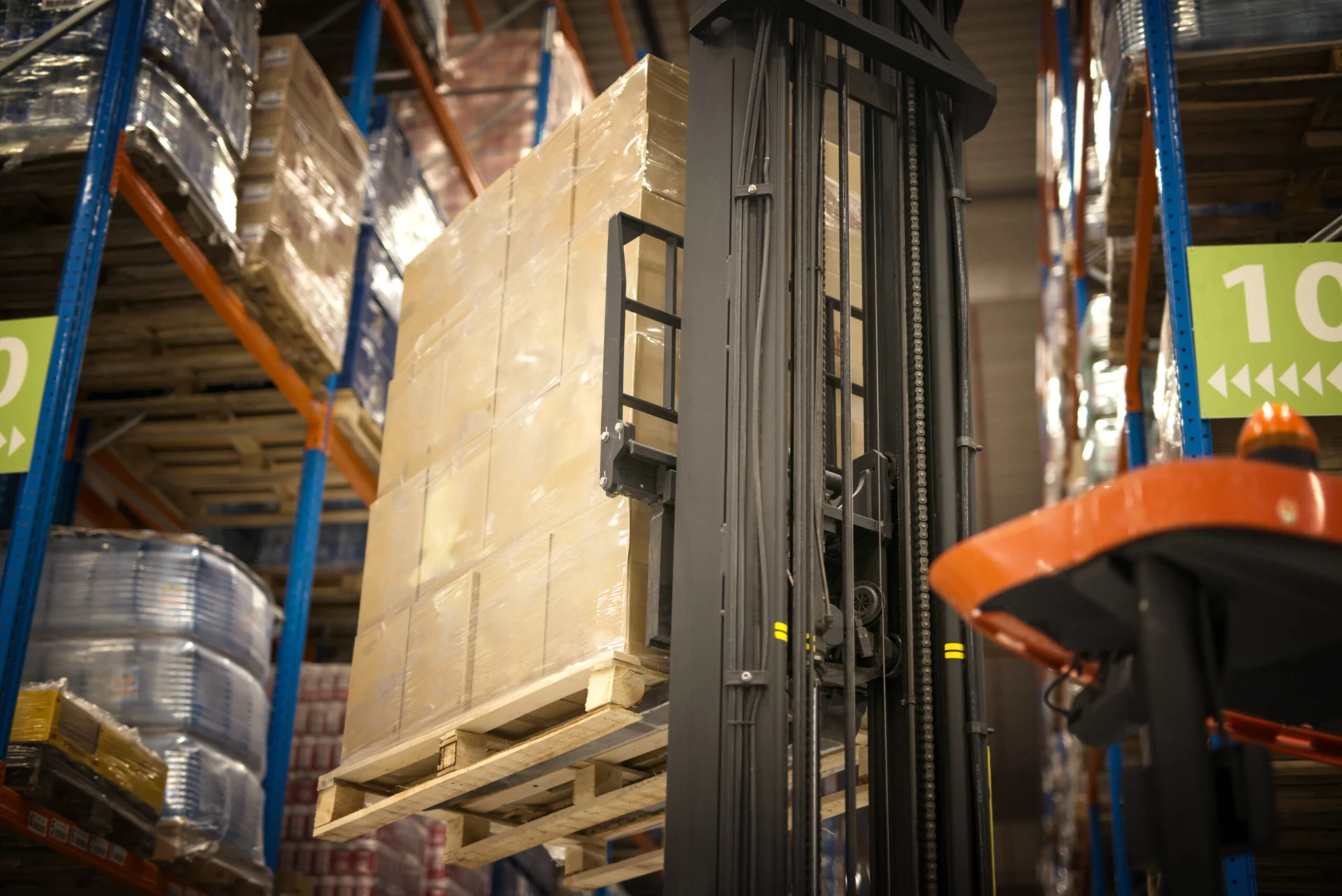Industrial Forklift Machine Lifting Palette Full Of Cardboard Boxes And Placing Them On Shelves In Distribution Warehouse Facility.